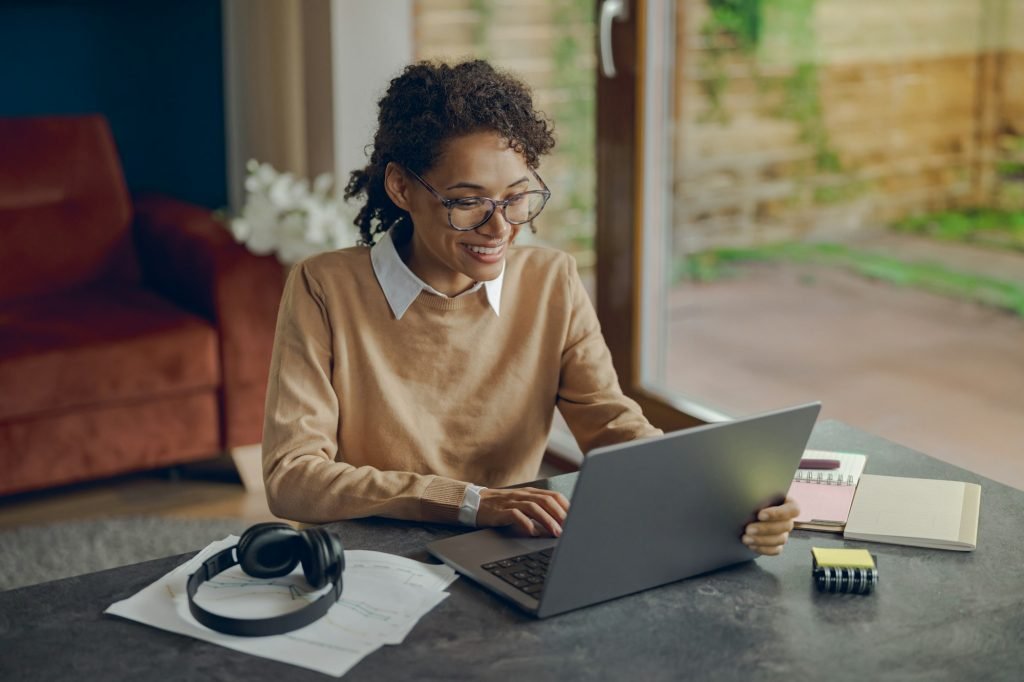 Smiling female manager working remotely on laptop from home while sitting at living room