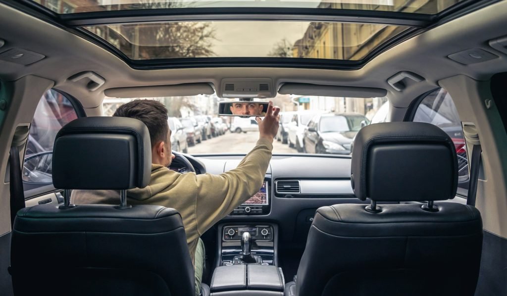 A male driver adjusts the mirror in the car.