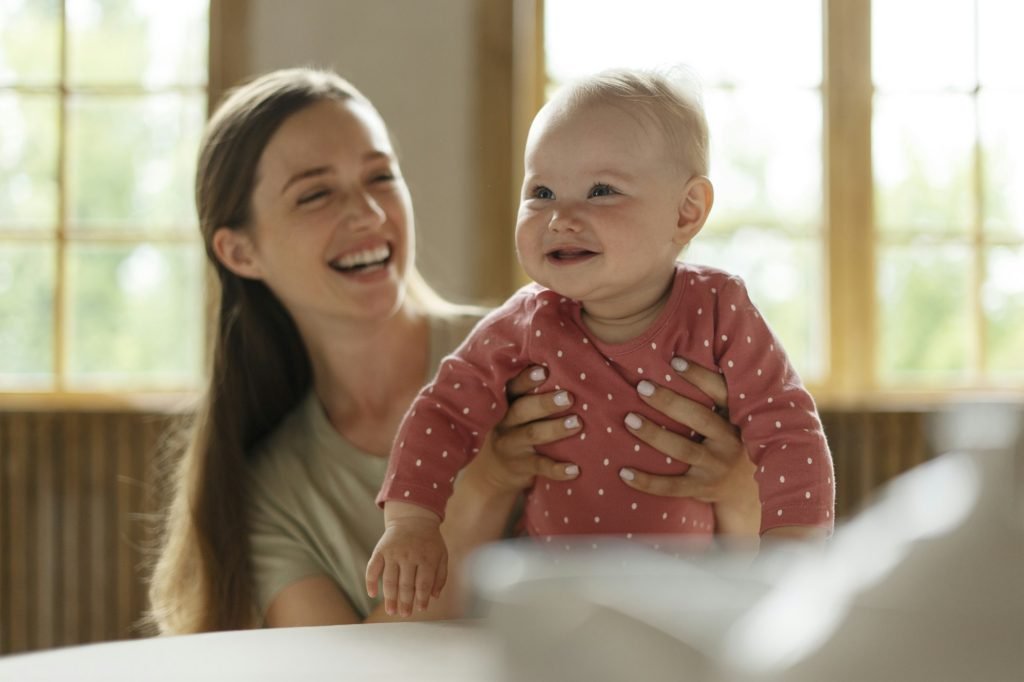Cute nanny takes care of adorable child in kindergarten, holding her, smiling