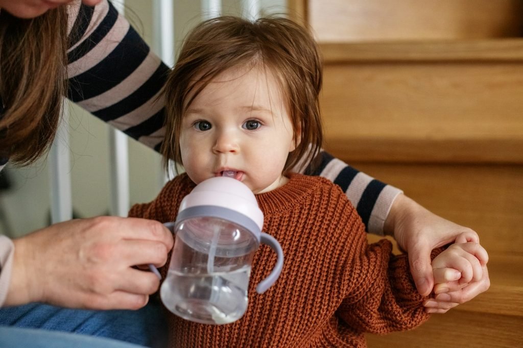 young mother feeding her baby with glass of water